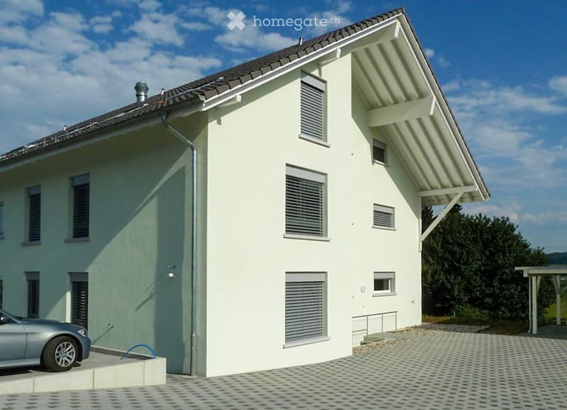 Two-story house with light green exterior, multiple windows, garage, and parking area.