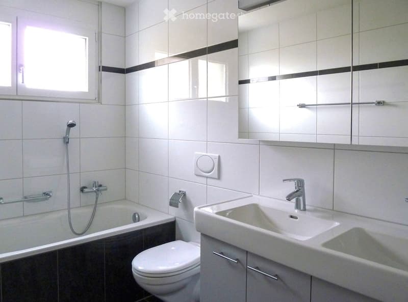 Modern bathroom with white tiles, bathtub, toilet, sink, mirror, and showerhead.