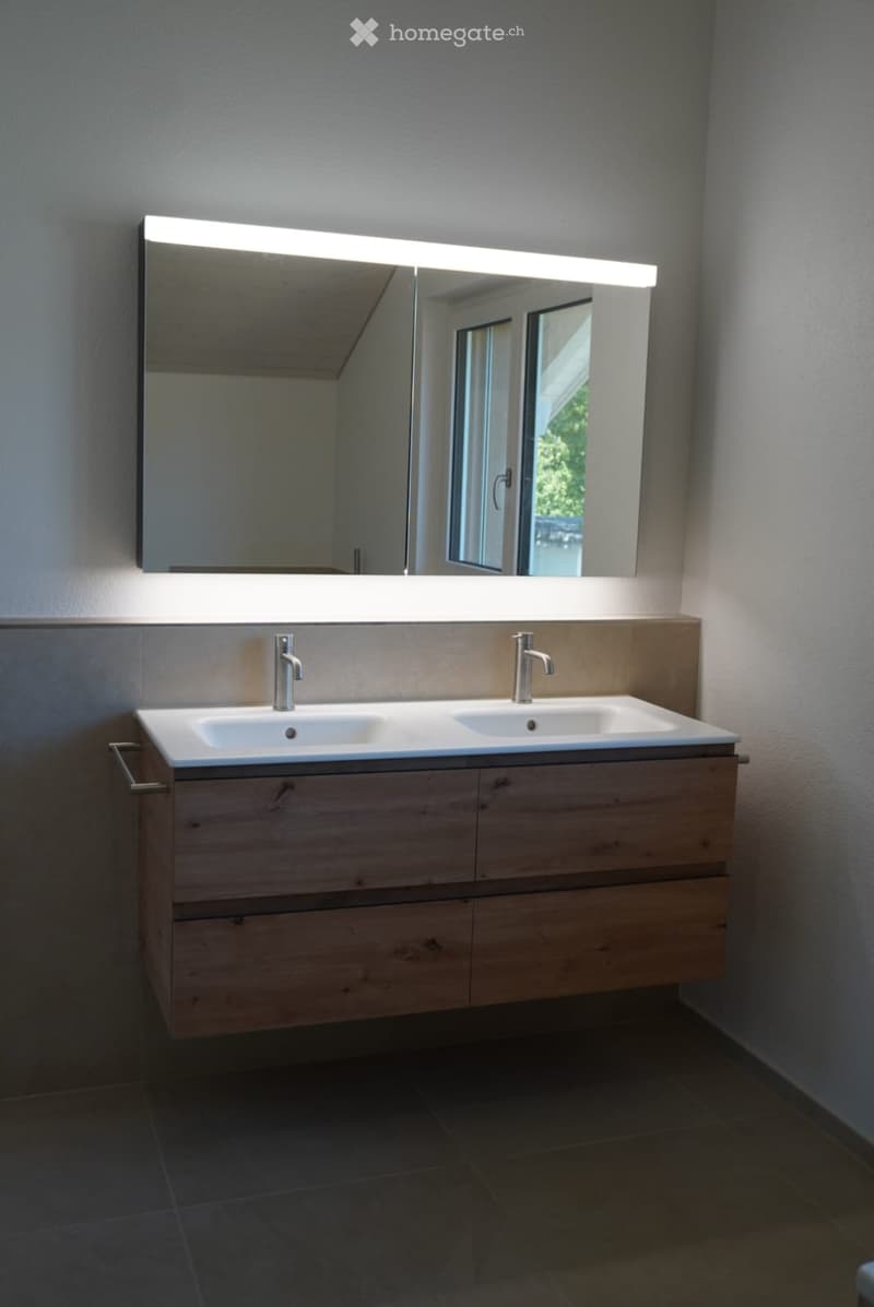 Modern bathroom with a double sink vanity, sleek wooden cabinet, and large mirror with built-in lighting.