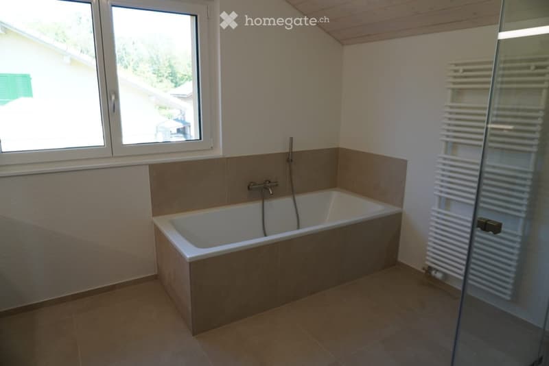 Modern bathroom with a bathtub, tiled walls, a radiator, and large windows offering a view of the outside.