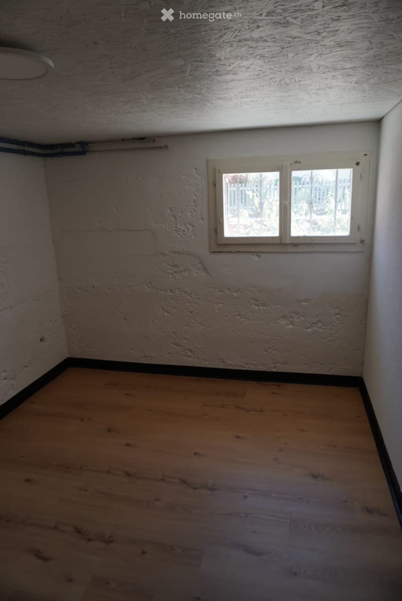 Empty room with wooden flooring, textured walls, and a single window with white frame and decorative glass panels.