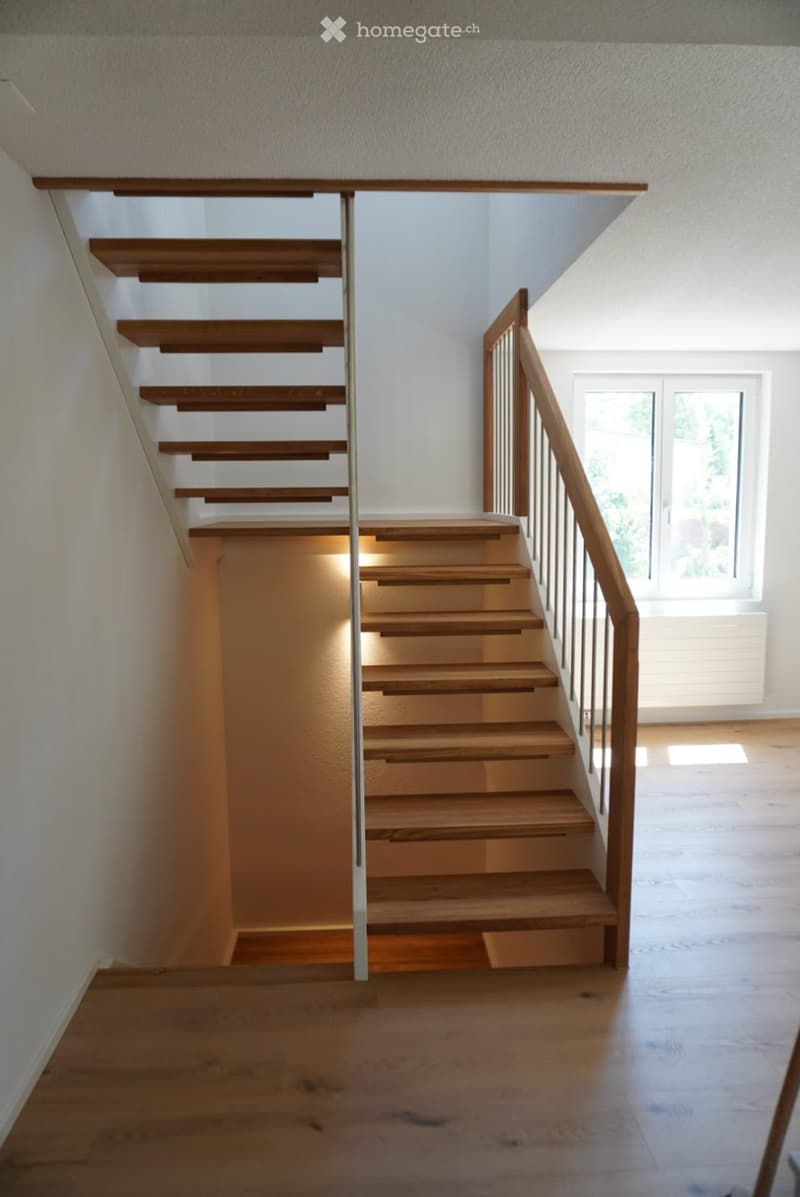 Wooden staircase with metal railing, illuminated steps, and a window at the end of the hallway.