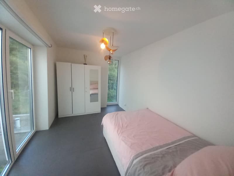 Modern bedroom with a double bed, white wardrobe, large windows, and a hanging lamp.