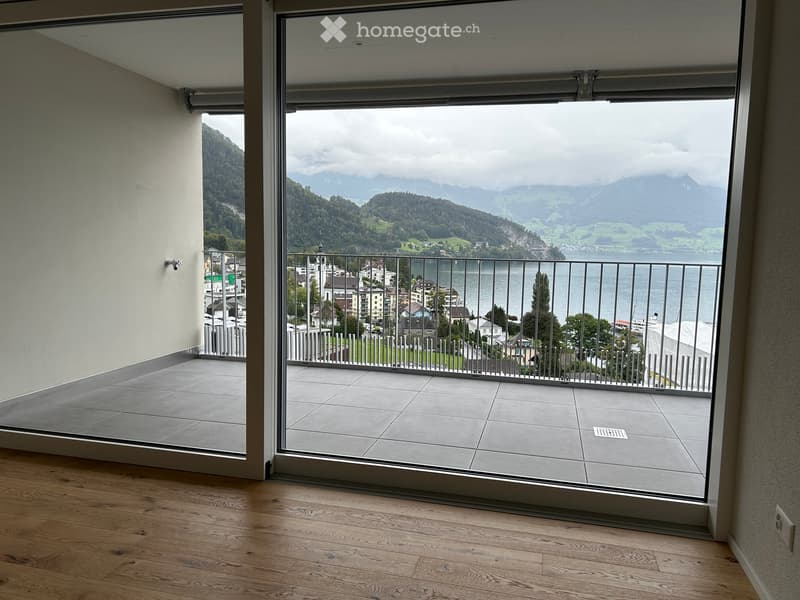 Balcony with large glass sliding doors, tiled floor, metal railing, overlooking a scenic lake and mountain landscape.
