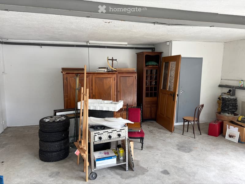 Garage with various stored items including cabinets, chairs, tires, a small table, and other miscellaneous objects.