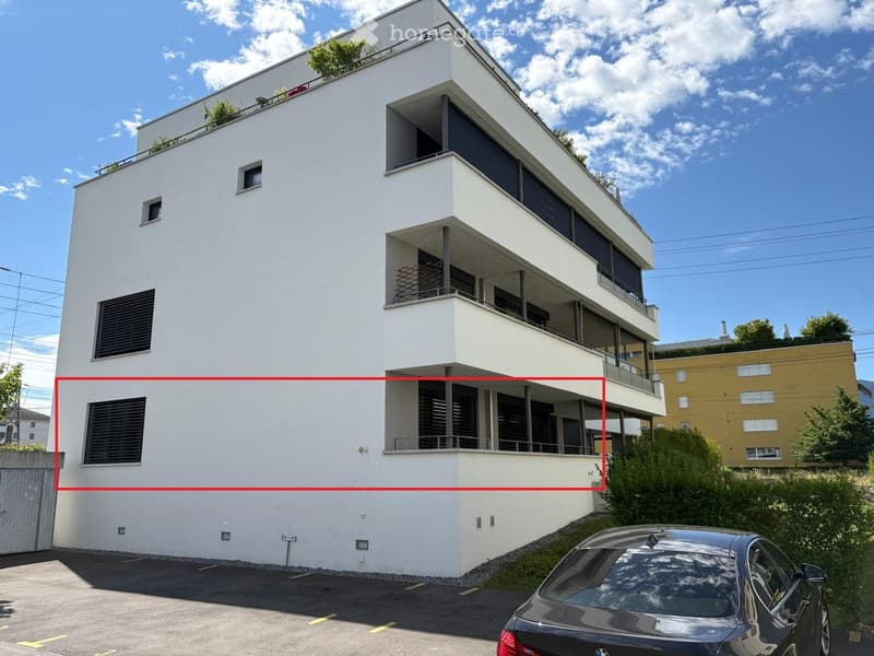 Modern multi-story building with white facade, large windows, balconies, and rooftop greenery.