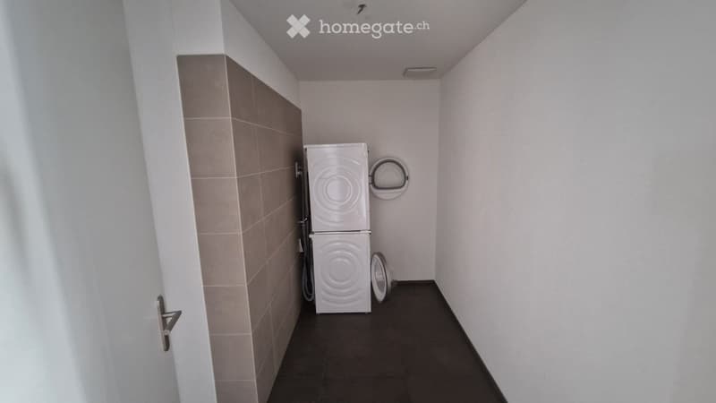 A small bathroom with a washing machine, a towel rack, and a dark tiled floor.