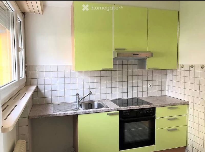 Modern kitchen with light green cabinets, tiled walls, granite countertops, and stainless steel appliances including a sink, faucet, and oven.