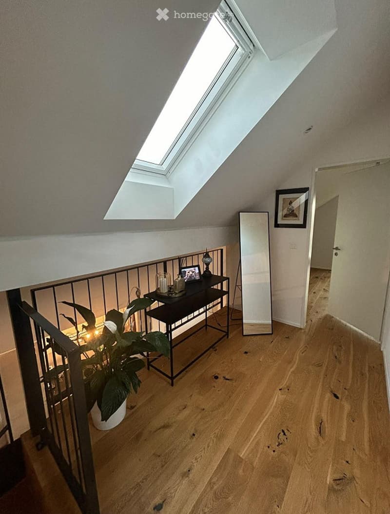 Attic room with wooden flooring, slanted ceiling, skylight window, small black table with decorative items, potted plant, and a mirror leaning against the wall.