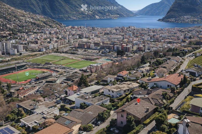 Aerial view of a town with numerous buildings, a football stadium, and a scenic lake in the background.