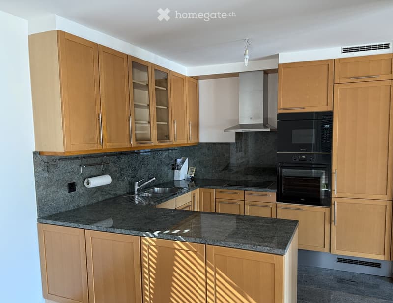 Modern kitchen with light wooden cabinets, granite countertops, stainless steel sink, and built-in oven and range hood.