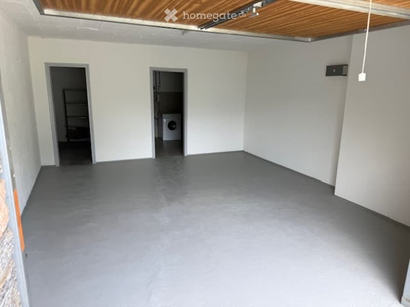 Empty room with grey concrete floor, white walls, and a washing machine in an adjacent space.