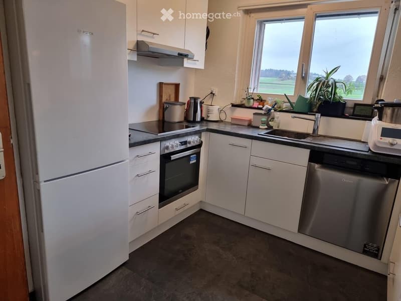 Modern kitchen with white cabinets, stainless steel appliances, and a black countertop. Features include a refrigerator, oven, dishwasher, sink, and various small appliances.