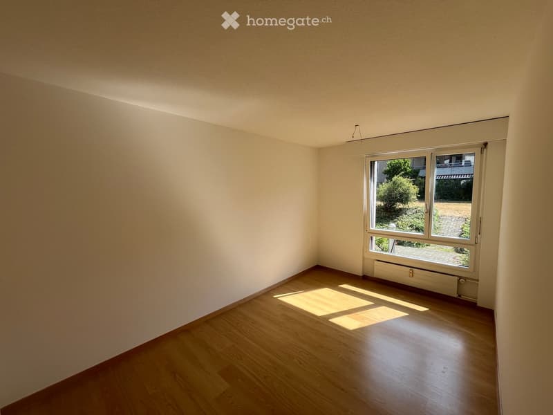 Empty room with wooden flooring and large windows, allowing natural light to fill the space.