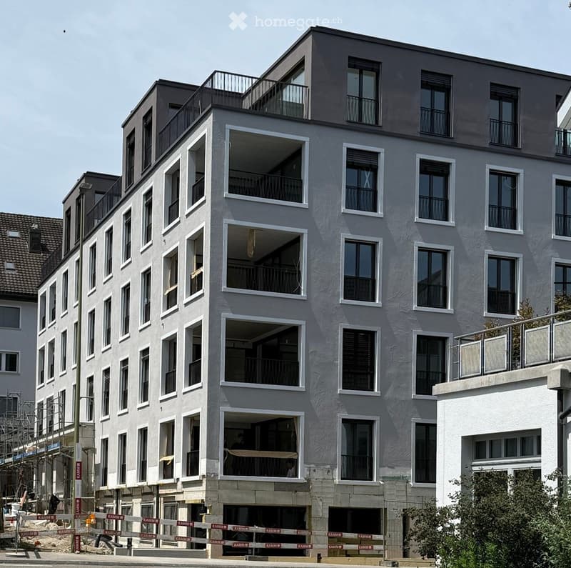 Modern multi-story residential building with grey facade, large windows, and multiple balconies.