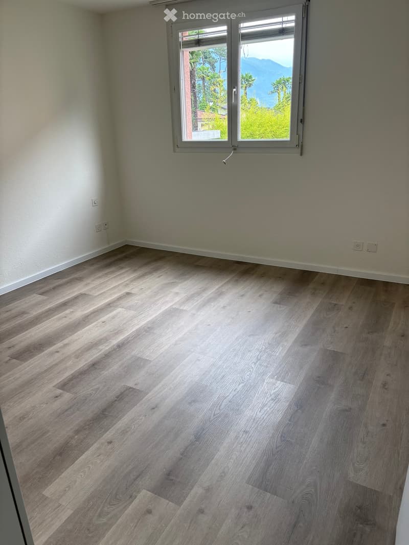 Empty room with light wooden flooring and white walls, featuring a large window with a scenic mountain view outside.