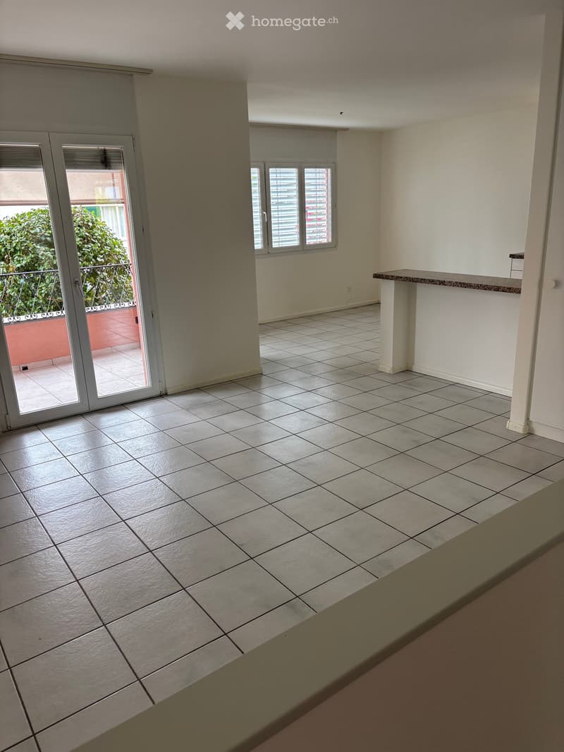 Empty room with tiled floor, white walls, large sliding glass door leading to a balcony, and a small window with blinds.