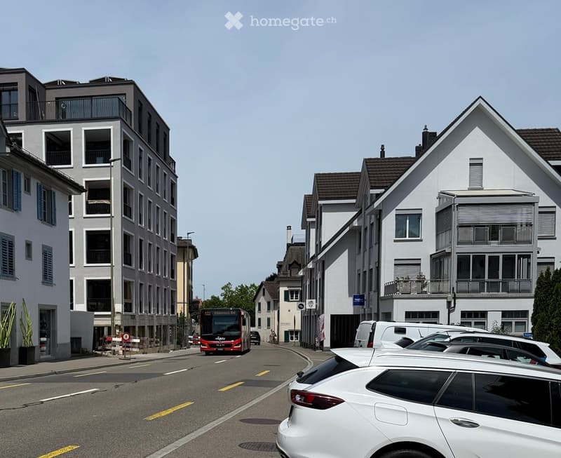 A street view showing a mix of modern and traditional buildings, with a bus and several parked cars visible.