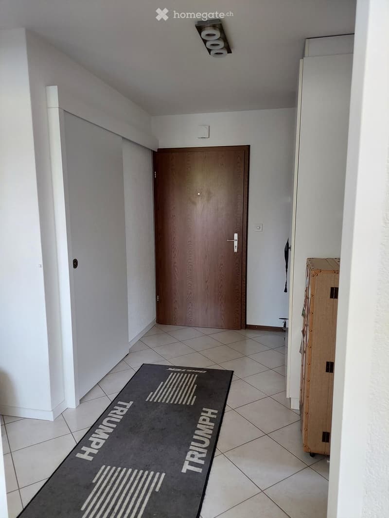 Empty hallway with tiled floor, white walls, a wooden door, and a black runner with the word "TRIUMPH" printed on it.