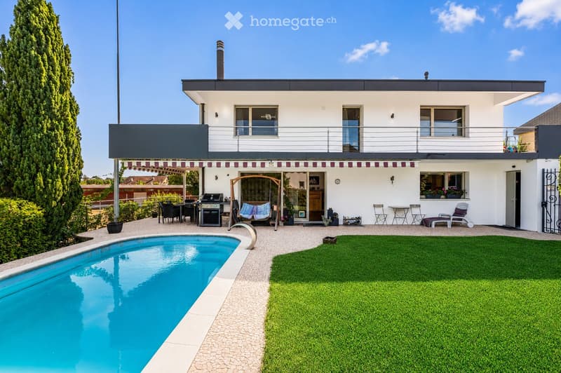 Modern two-story house with a swimming pool, patio furniture, and a well-maintained lawn.