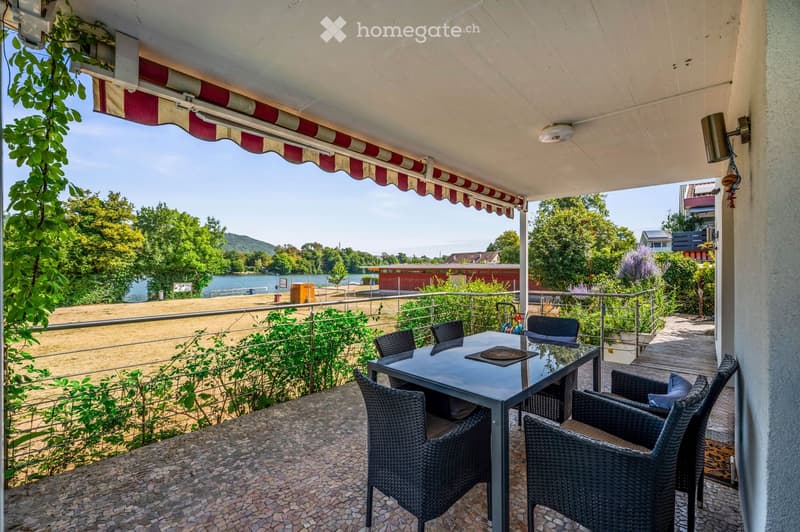 Balcony with a table and chairs, overlooking a scenic view of a river and greenery.