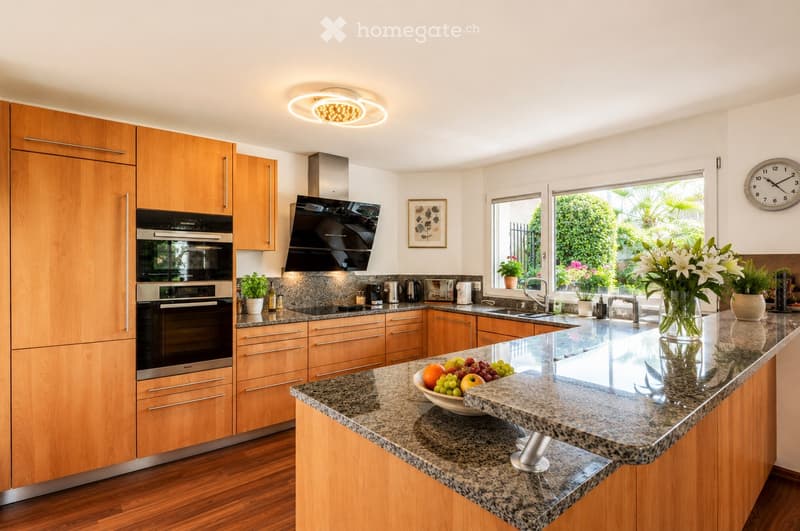 Modern kitchen with wooden cabinets, granite countertops, stainless steel appliances, and a central island with a bowl of fruit.