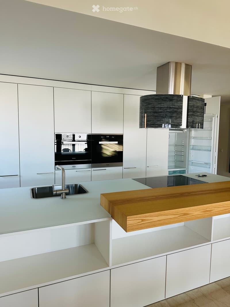 Modern kitchen with white cabinets, stainless steel appliances, a central island with a wooden countertop, and a sleek sink area.