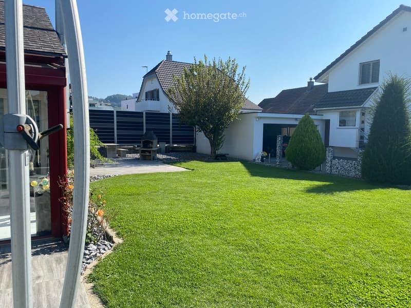 Well-maintained lawn with surrounding trees, a barbecue area, and a modern house in the background.