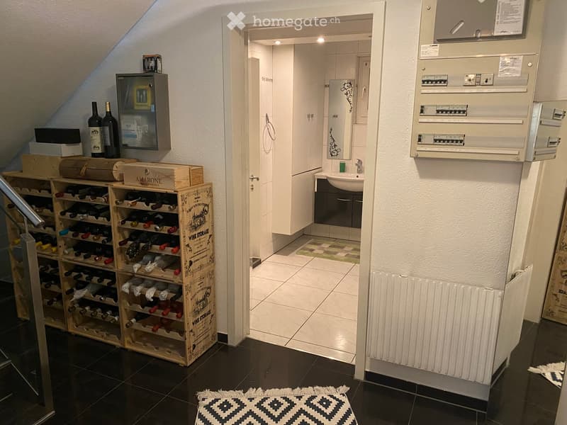 Hallway with a wine rack, small bathroom, and electrical panel. The hallway features dark tiled flooring, white walls, and a patterned rug.