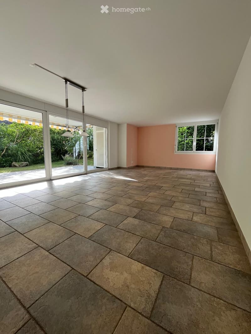 Empty room with tiled floor, white walls, large sliding glass doors leading to a garden, and a window with white frame.