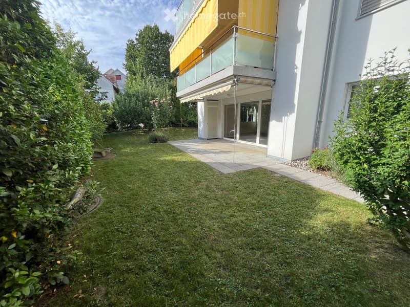 Well-maintained lawn with trimmed hedges and a modern house with a balcony and glass doors.