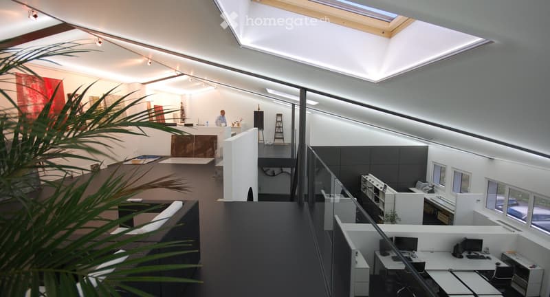 Modern office space with desks, chairs, screens, a sofa, and a reception area.