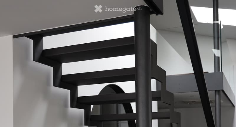 Modern black staircase with sleek design and glass railings, leading upwards in a well-lit interior space.
