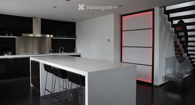 Modern kitchen with white island, black stools, stainless steel appliances, and sleek design.