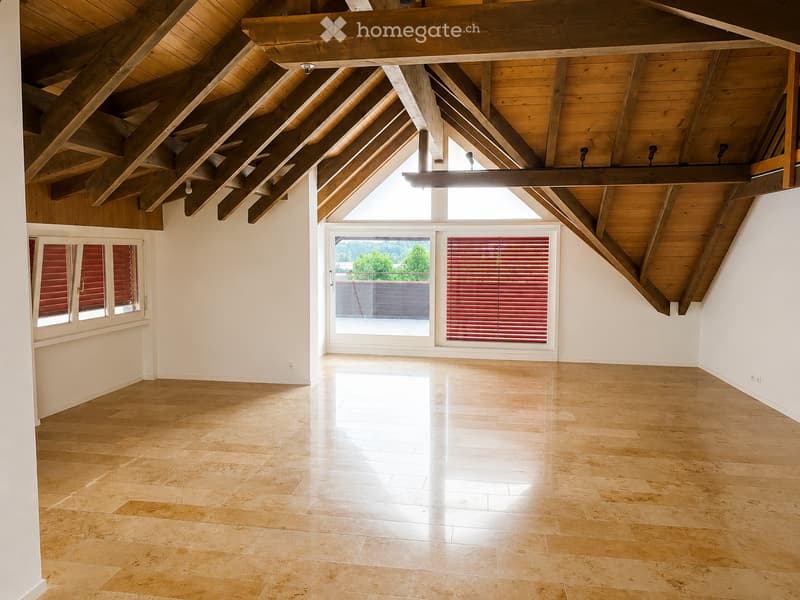 Bright, open room with wooden ceiling beams, large windows, and light-colored tile flooring. No furniture or furnishings are present.