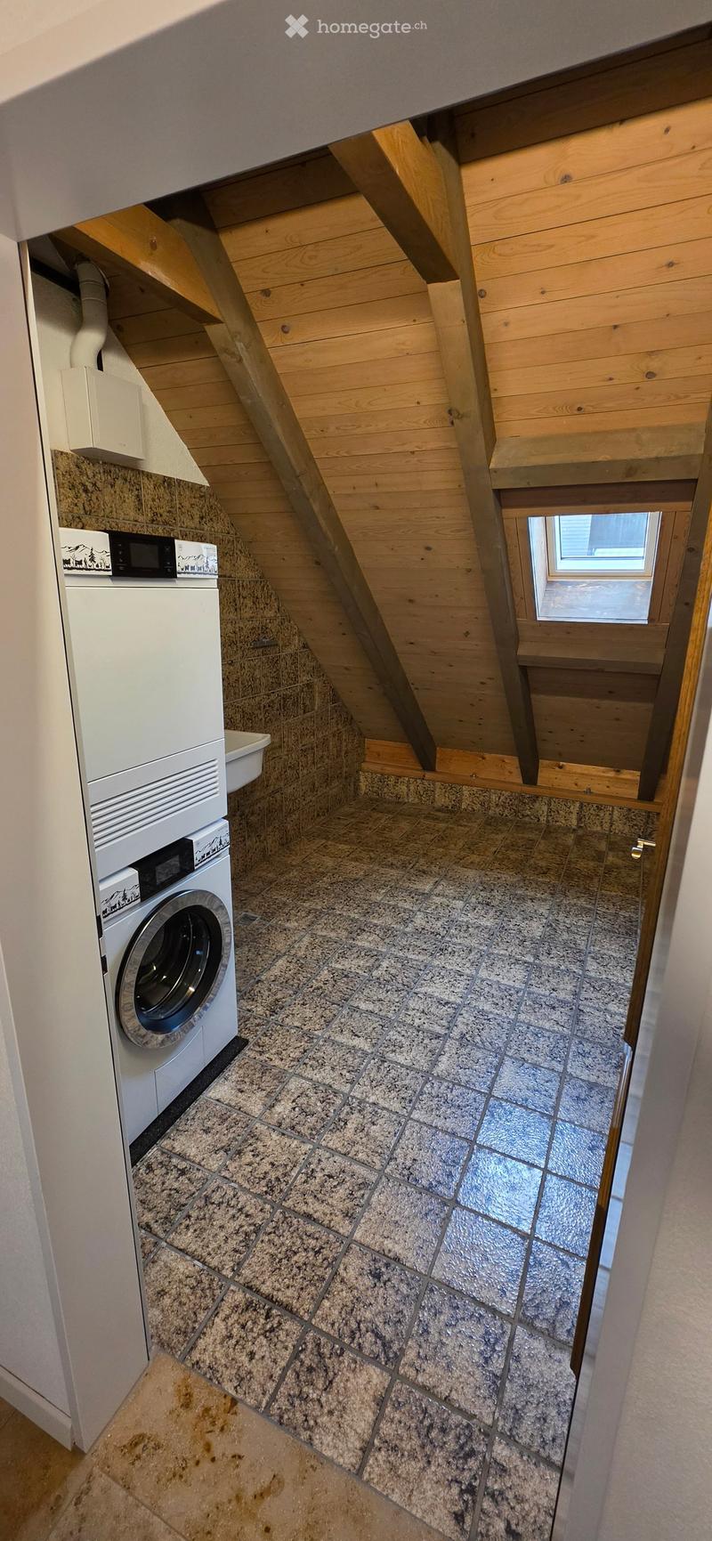 Attic bathroom with a washing machine, granite tiled floor, wooden ceiling beams, and a small window.