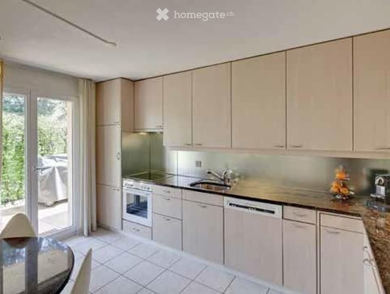 Modern kitchen with light-colored cabinets, stainless steel appliances, and a large window offering a view of the garden.