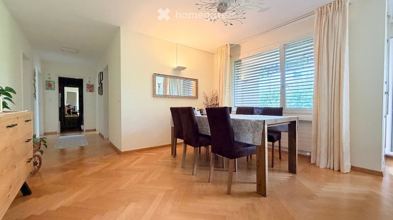 Dining room with wooden flooring, a dining table with chairs, a mirror on the wall, and a plant on a cabinet.