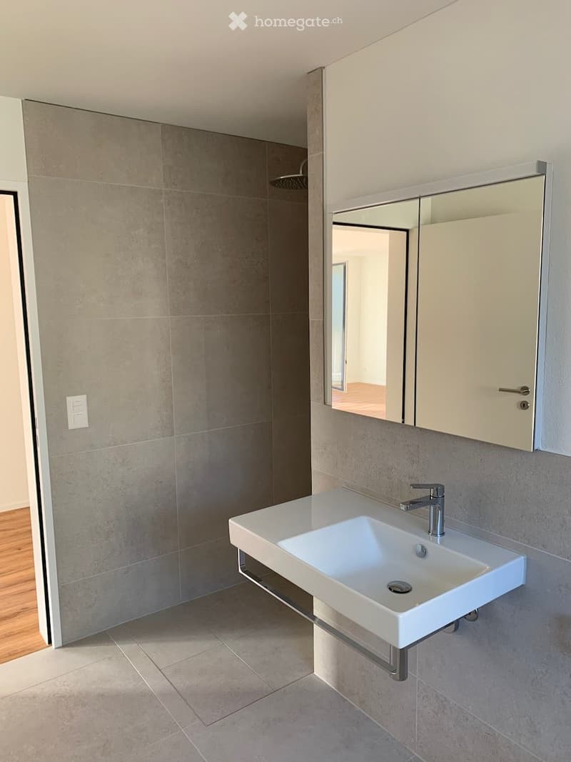 Modern bathroom with a white sink, chrome faucet, mirrored cabinet, and tiled walls.