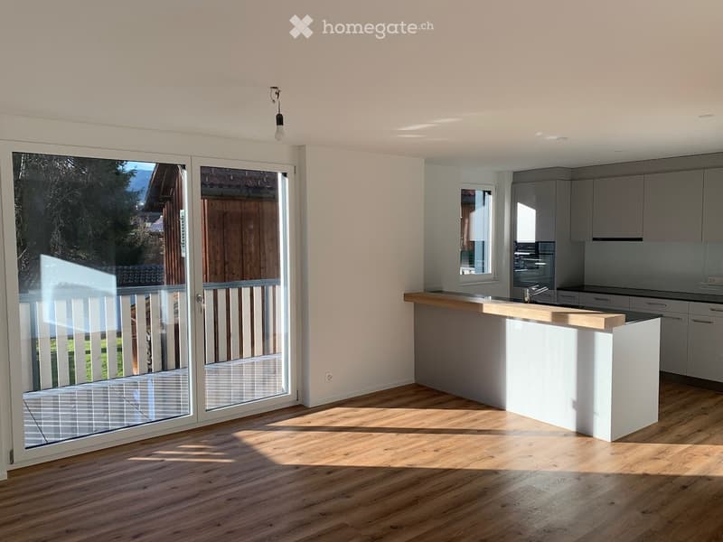 Modern kitchen with light wooden flooring, white walls, and a kitchen island with a wooden countertop. Large sliding glass doors lead to an outdoor area.