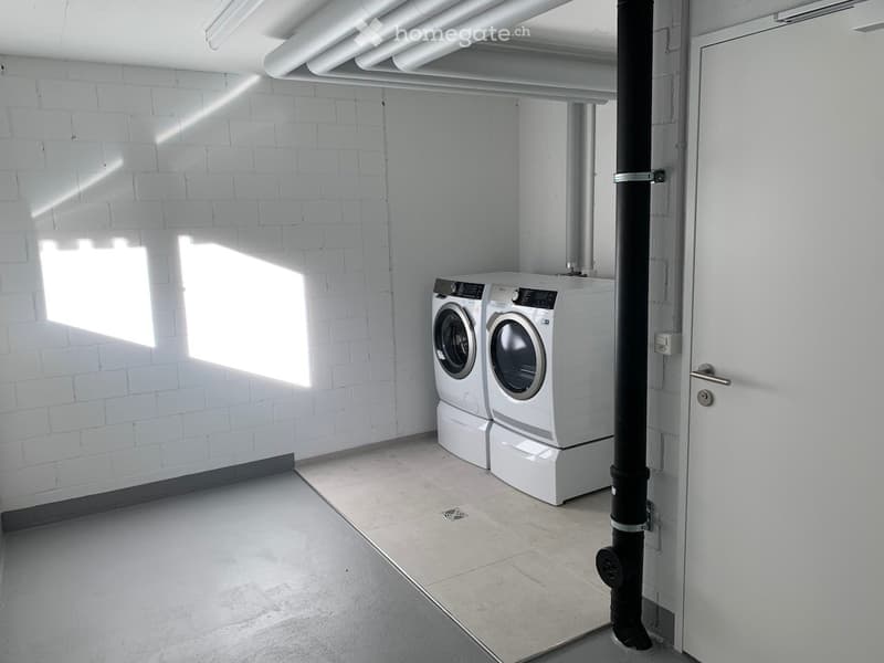 A clean, modern laundry room with white brick walls, tiled floor, and two stacked washing machines and dryers.
