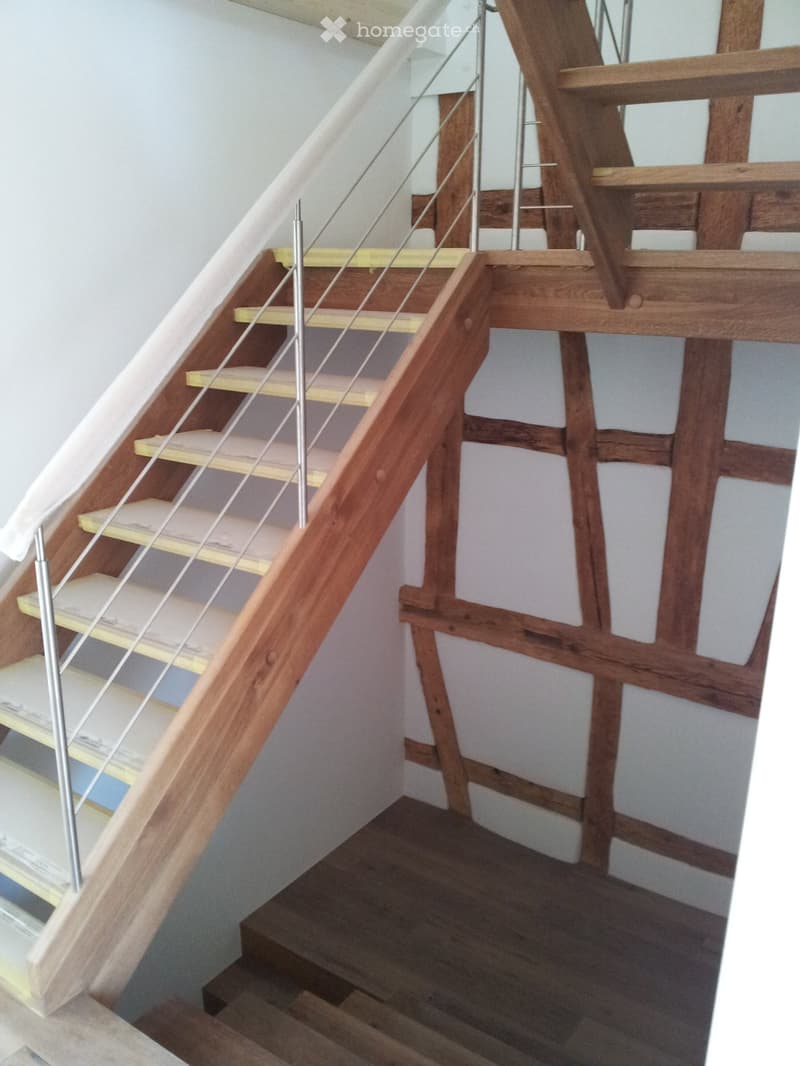 Wooden staircase with metal railing, light-colored steps, and exposed wooden beams in the background.