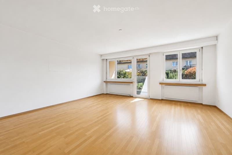 Empty room with light wooden flooring, white walls, large windows, and radiators beneath the windows.