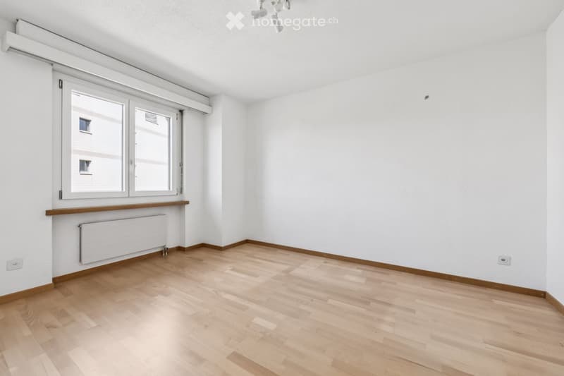 Empty room with light wooden flooring, white walls, and large windows with blinds. No furniture or equipment present.