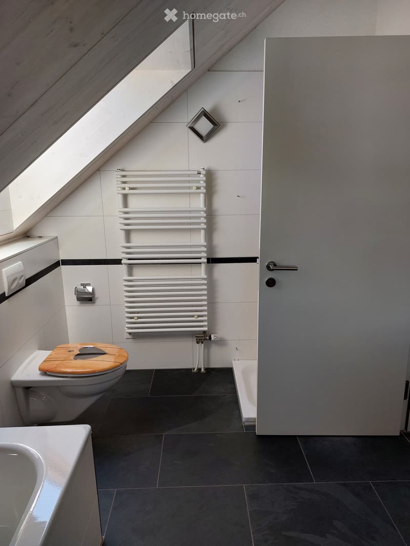 Modern bathroom with dark tiled floor, white radiator, wooden toilet seat, bathtub, and sink.