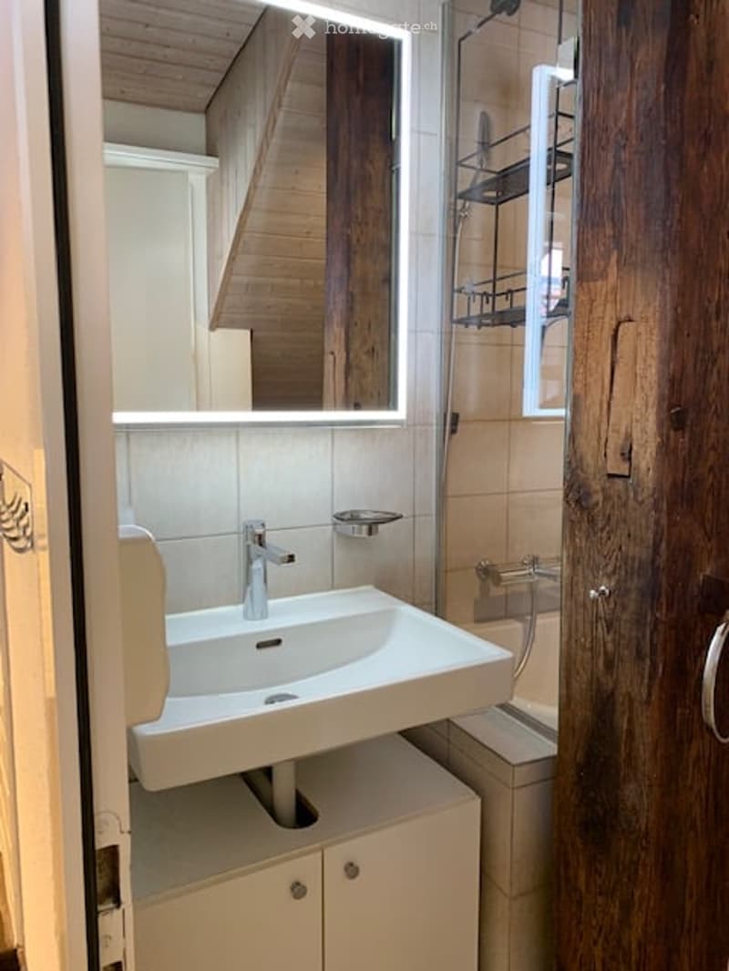 Modern bathroom with a white sink, sleek faucet, large mirror with LED lighting, and wooden cabinetry.