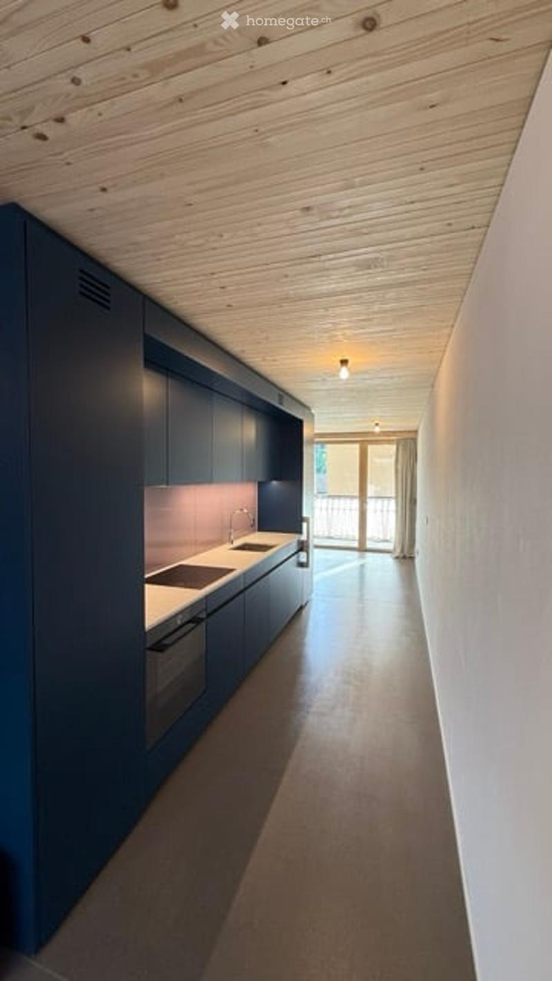 Modern kitchen with dark blue cabinets, white countertops, and a sleek design. Features a sink, faucet, and built-in oven. The space has a clean, minimalist aesthetic with a view to a balcony through large glass doors.