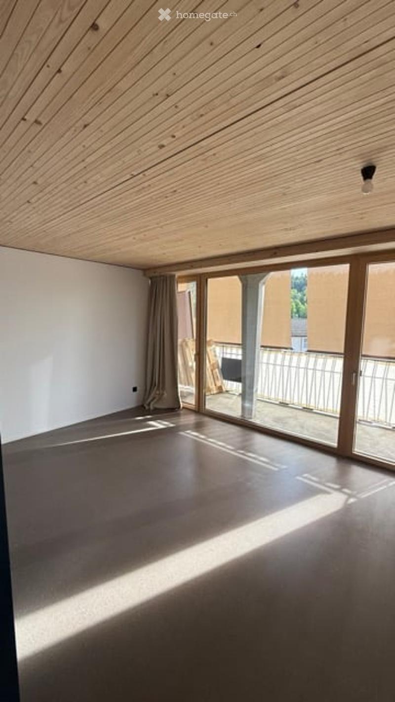 Empty room with wooden ceiling, large sliding glass doors leading to a balcony, and grey concrete floor.