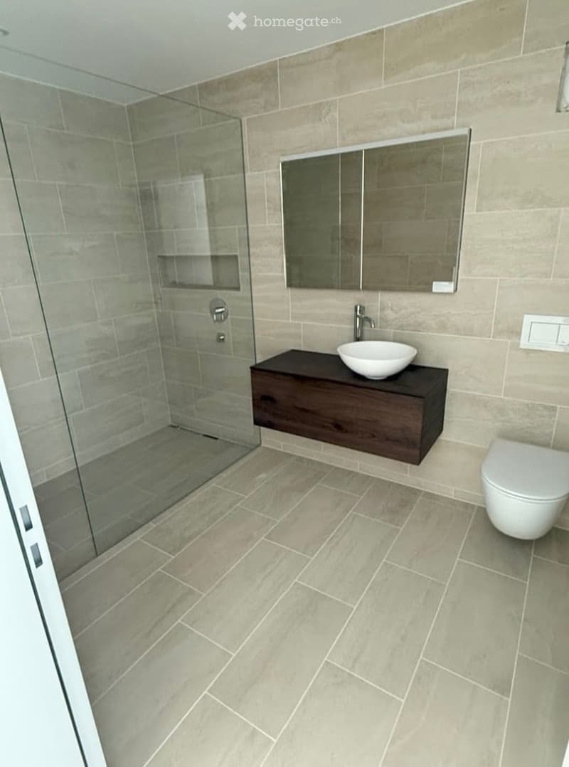 Modern bathroom with beige tiles, a dark wooden vanity, a white sink, a toilet, and a glass-enclosed shower.