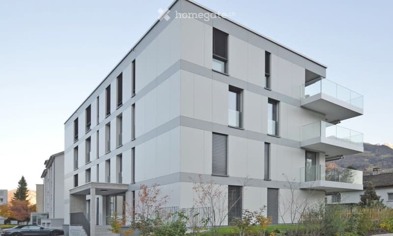 Modern multi-story residential building with white and grey facade, multiple balconies, and large windows.